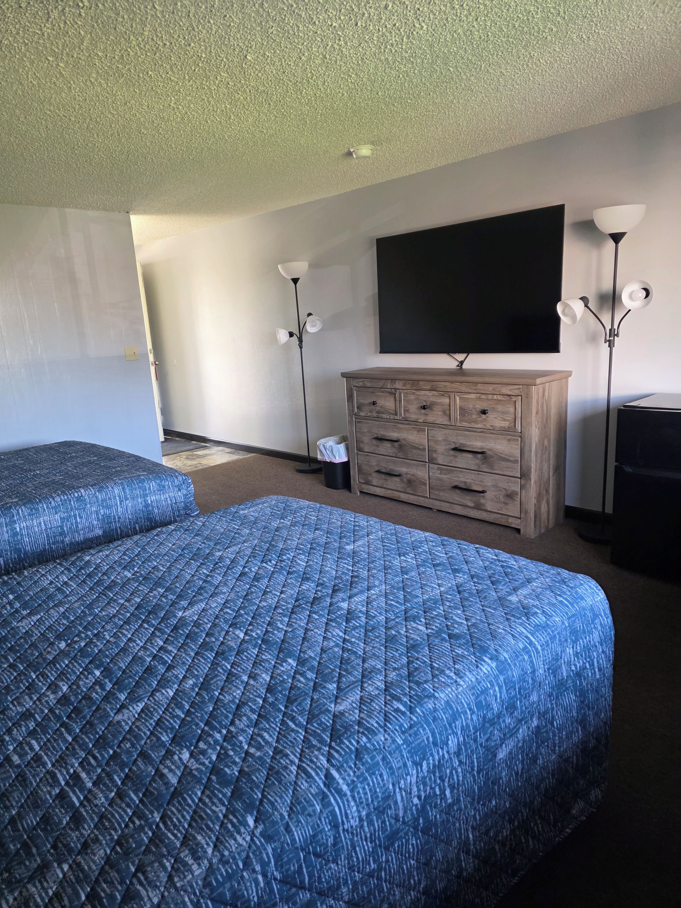 A hotel room with two beds, a wooden dresser, a flat-screen TV, and two floor lamps.
