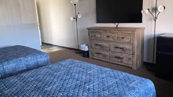 A hotel room with two beds, a wooden dresser, a flat-screen TV, and two floor lamps.