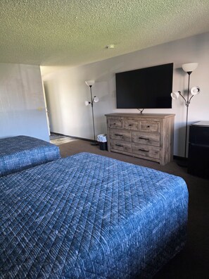A hotel room with two beds, a wooden dresser, a flat-screen TV, and two floor lamps. - Fort Union Inn (Colstrip)