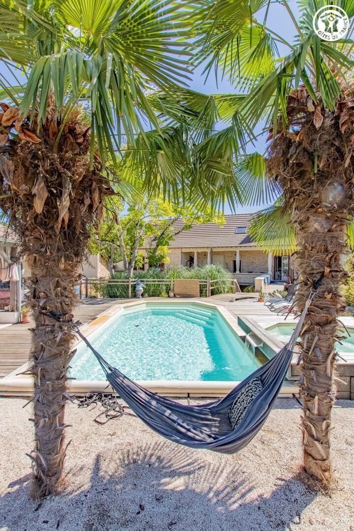 Un espace piscine avec un hamac, des palmiers et un bâtiment en arrière-plan.
