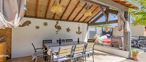 Une terrasse extérieure avec une table et des chaises en bois, des éléments décoratifs muraux et une structure en forme de pergola.