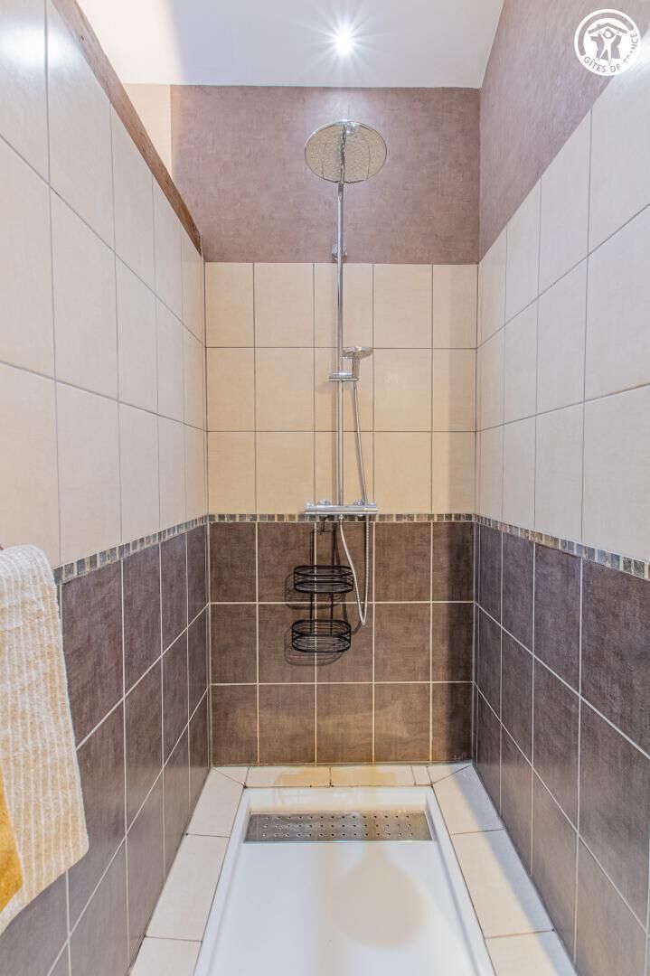 A shower with a ceiling-mounted rain showerhead, a towel rack, and a tiled floor.