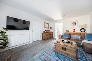 Ein Wohnzimmer mit einem Flachbildfernseher, einer Holzeinrichtung, einem braunen Ledersofa und einem gemusterten Teppich.