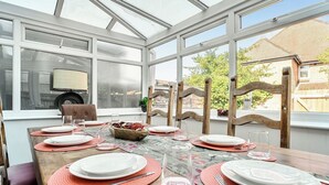 Ein Wintergarten mit einem Esstisch, gedeckt für sechs Personen, umgeben von Holzstühlen.