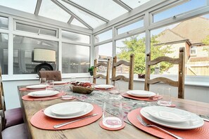 Ein Wintergarten mit einem Esstisch, gedeckt für sechs Personen, umgeben von Holzstühlen.
