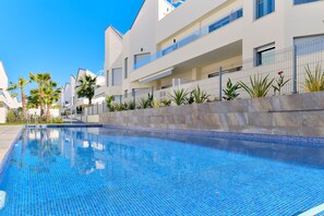 Un edifici residencial modern amb piscina, envoltat de palmeres i una paret de pedra.