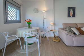 Ett modernt vardagsrum med ett runt matbord, vita stolar, en beige soffa och en golvlampa.