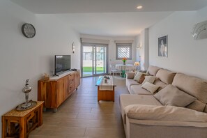 A modern living room with a sofa, television, wooden cabinet, and a dining area with a table and chairs. - Villa Amalia 9: Ground floor with garden (Torrevieja)