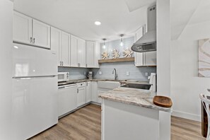 Uma cozinha moderna com armários brancos, bancada de mármore e forno embutido.