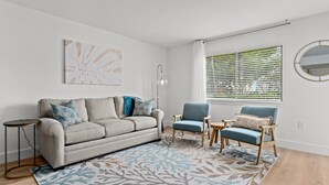 A modern living room with a grey sofa, two blue armchairs, a patterned rug, and a large window with blinds. - CLM 16B  Gorgeous, pet friendly - Private beach access (Destin)
