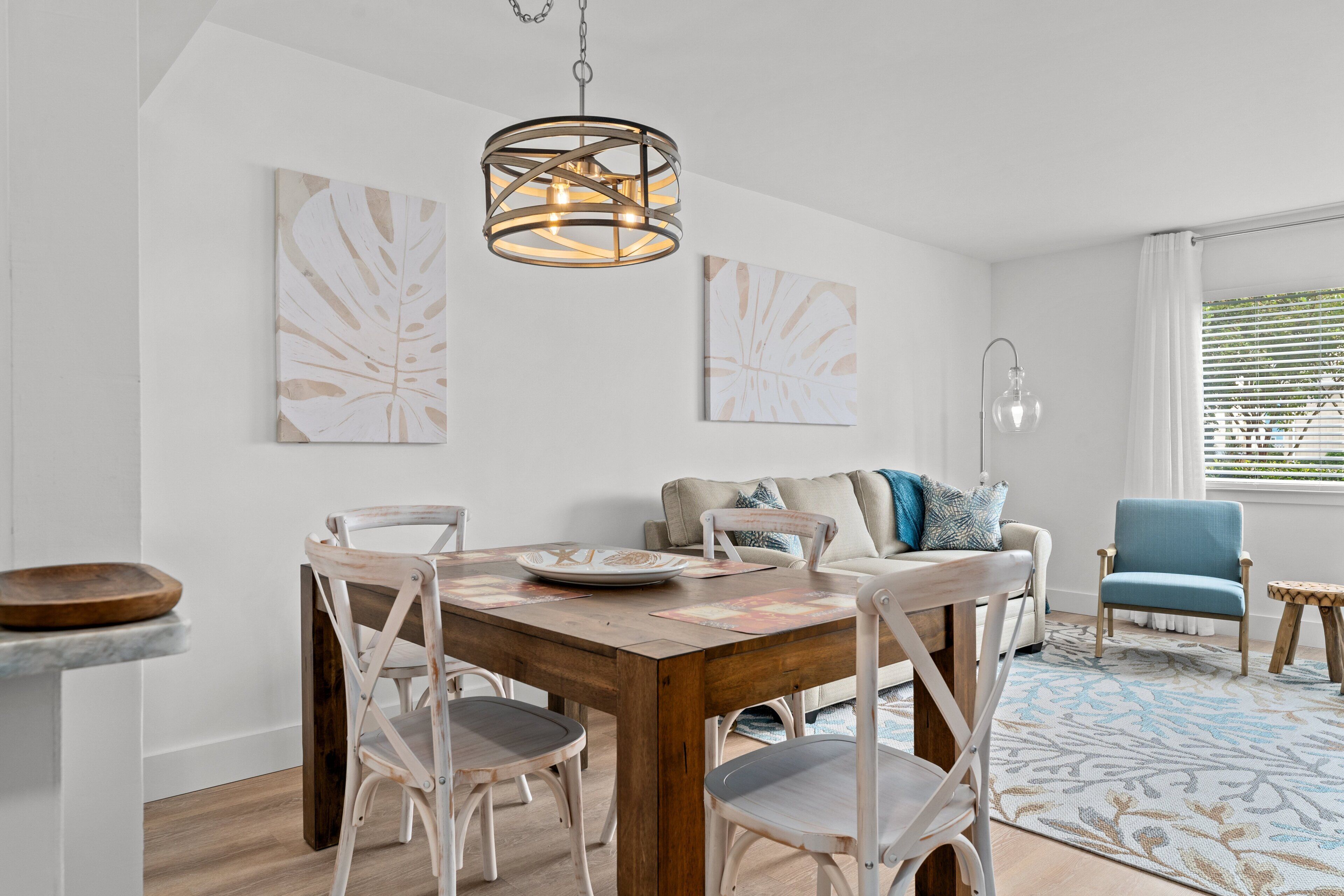 A dining area with a wooden table, white chairs, and a hanging light fixture.