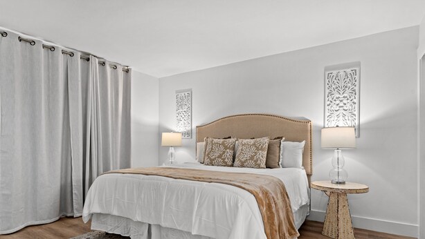 A bedroom with a large bed, two bedside tables with lamps, a decorative wall panel, and a patterned rug. - CLM 16B  Gorgeous, pet friendly - Private beach access (Destin)