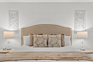Quarto com uma cama grande, duas luminárias de cabeceira e painéis decorativos na parede.