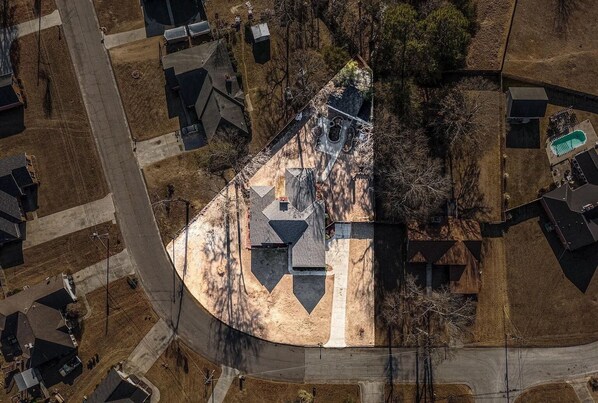 An aerial view of a residential area with a prominent house featuring a unique triangular roof design, surrounded by other houses and a clear sky.