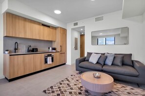 A modern kitchen with wooden cabinets, a built-in oven, and a coffee machine. There is a grey sofa with cushions and a patterned rug in the living area. - Cozy 1-bedroom studio in lovely Miami (Miami)