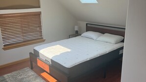 Ein Schlafzimmer mit Dachfenster, einem Bett, einem Nachttisch, einer Lampe und einem Teppich.