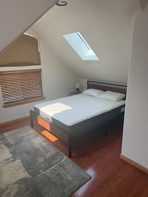 A bedroom with a skylight, a bed, a nightstand, a lamp, and a rug. - Charming 2-bedroom building in peaceful Spangle with AC (Spangle)