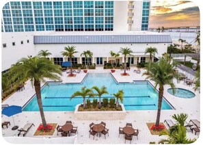 Um hotel com uma grande piscina ao ar livre, palmeiras e vista para o oceano.