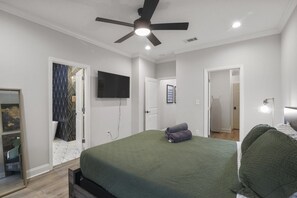 Ein Schlafzimmer mit einem Bett, einem Deckenventilator, einem Flachbildfernseher und einer Tür zu einem anderen Raum.