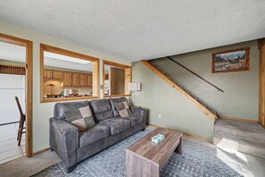 A living room with a gray sofa, wooden coffee table, and a staircase leading to a kitchen. - 1 minute to Yellowstone Trpper Unit 2 (West Yellowstone)