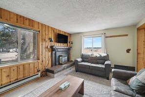 A room with a fireplace, a sofa, a coffee table, and a large window. - 1 minute to Yellowstone Trpper Unit 2 (West Yellowstone)