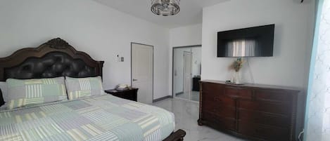 A bedroom with a bed, dresser, TV, and a door leading to another room.