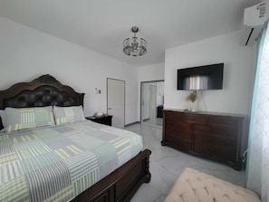 A bedroom with a bed, dresser, TV, and a door leading to another room. - 3 Bedroom Luxe Hideaway in Ocho Rios with Pool Access (Ocho Rios)