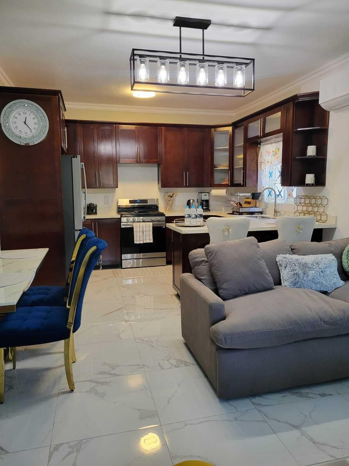 A modern kitchen with dark wood cabinets, a stainless steel stove, and a dining area with a blue upholstered chair.