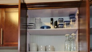 Et køkken med komfur, kaffemaskine og et skab med tallerkener og glasbeholdere.