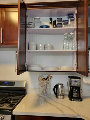 Eine Küche mit Herd, einer Kaffeemaschine und einem Schrank mit Geschirr und Gläsern.