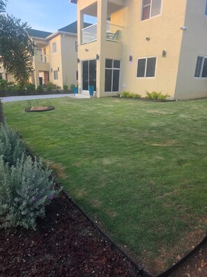Ein Wohngebäude mit gepflegtem Rasen, einem kleinen Gartenbereich mit Sträuchern und blauem Himmel.