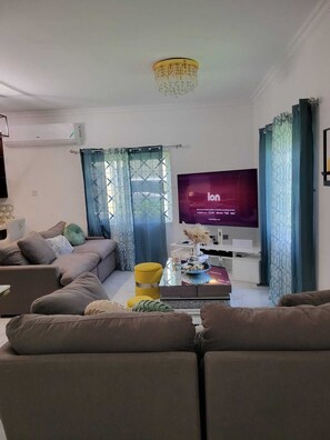 A living room with a sofa, a coffee table, a television, and a decorative chandelier. - 3 Bedroom Luxe Hideaway in Ocho Rios with Pool Access (Ocho Rios)