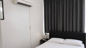 Ein Hotelzimmer mit einem Bett, einem Nachttisch, einer Lampe, einer Klimaanlage und einem Fenster mit Vorhängen.