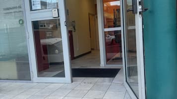 A hotel entrance with glass doors, a tiled floor, and a teal-colored wall.