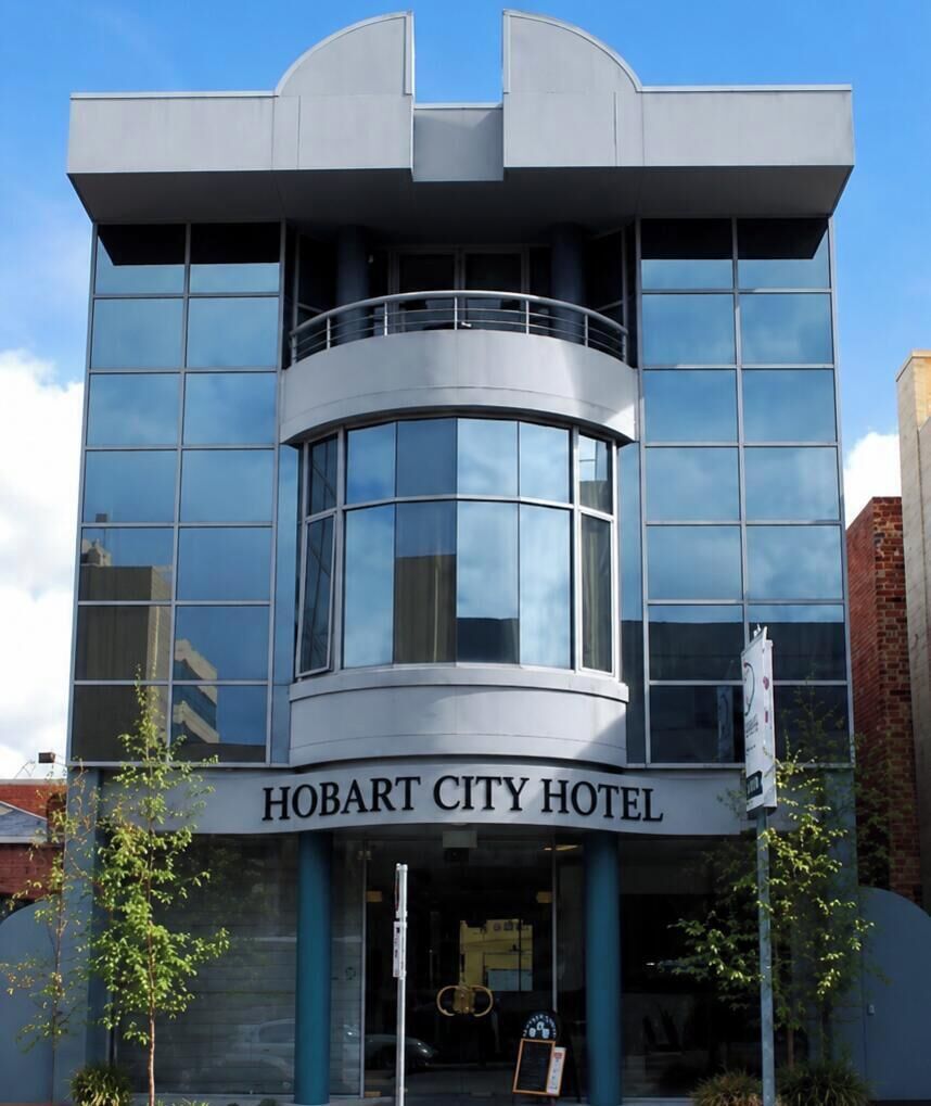 A modern building with a curved glass facade, a prominent entrance, and a sign reading 'HOBART CITY HOTEL'.