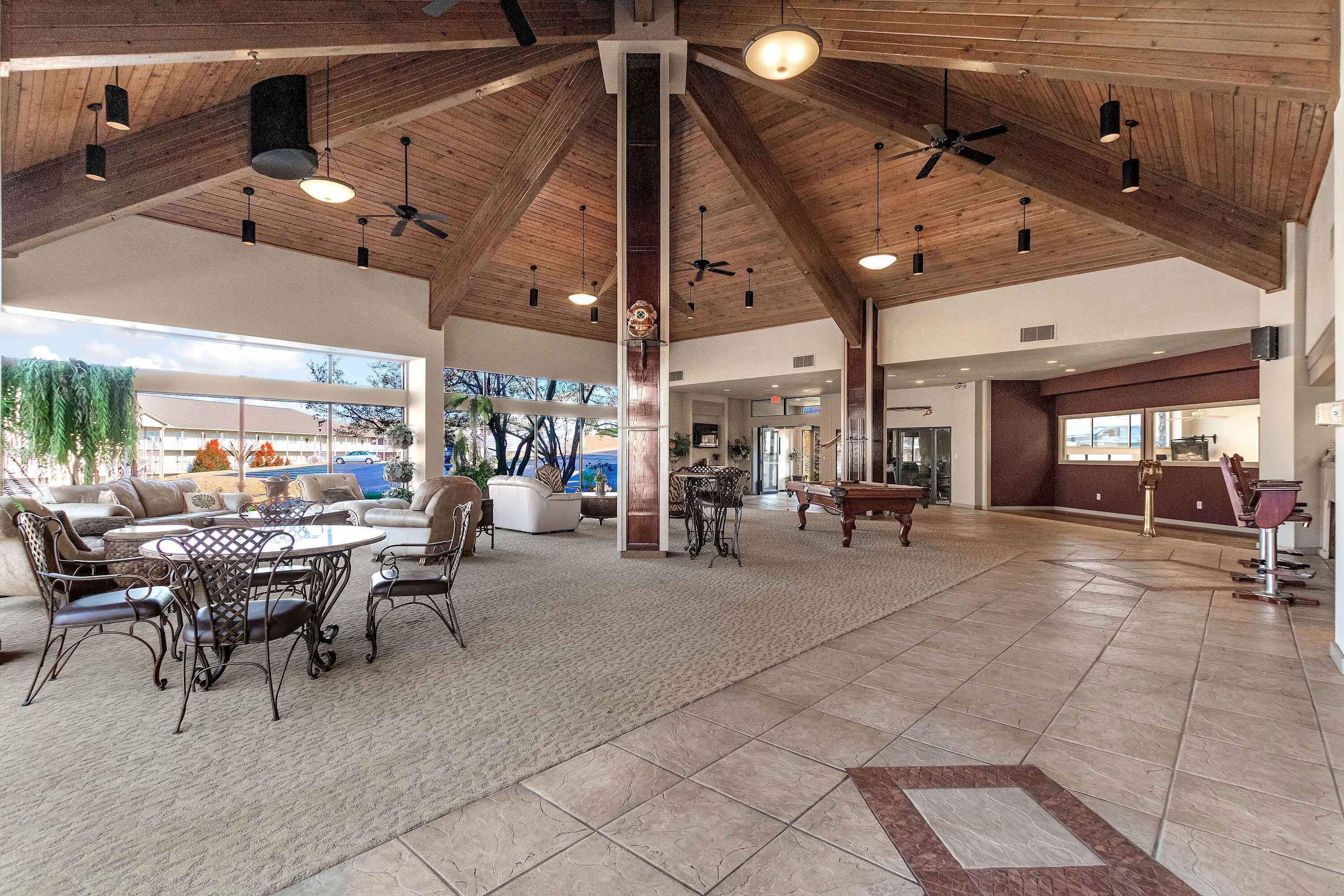 A spacious indoor area with a high ceiling, wooden beams, and a central column. There are multiple seating areas with tables and chairs, and a reception desk is visible in the background.