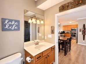 A modern bathroom with a large mirror, a sink, and a toilet. There is a wooden cabinet with drawers and a towel rack. A sign on the wall reads 'Lake life.' - Eagles Nest @ Lands End - Boat Slip! (Osage Beach)