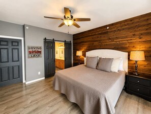 Ein Schlafzimmer mit einem Bett, zwei Nachttischlampen, einem Deckenventilator und einer Holzwand.