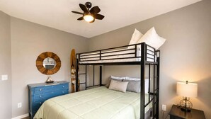 Ein Schlafzimmer mit Etagenbett, Kommode, Lampe und Deckenventilator.
