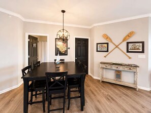 A dining room with a black table and chairs, a chandelier, and a wall with two paddleboards and two framed pictures. - Eagles Nest @ Lands End - Boat Slip! (Osage Beach)