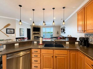 A modern kitchen with a central island, stainless steel appliances, wooden cabinets, pendant lighting, and a view to the outdoors. - Eagles Nest @ Lands End - Boat Slip! (Osage Beach)