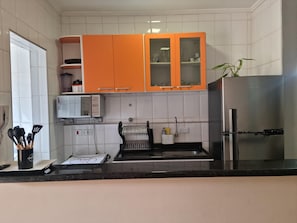 A kitchen with white tiled walls, a stainless steel refrigerator, and orange cabinets. - Apto Confortável em Ubatuba a 4 Min da Praia das Toninhas com Wi-Fi e Garagem (Ubatuba)