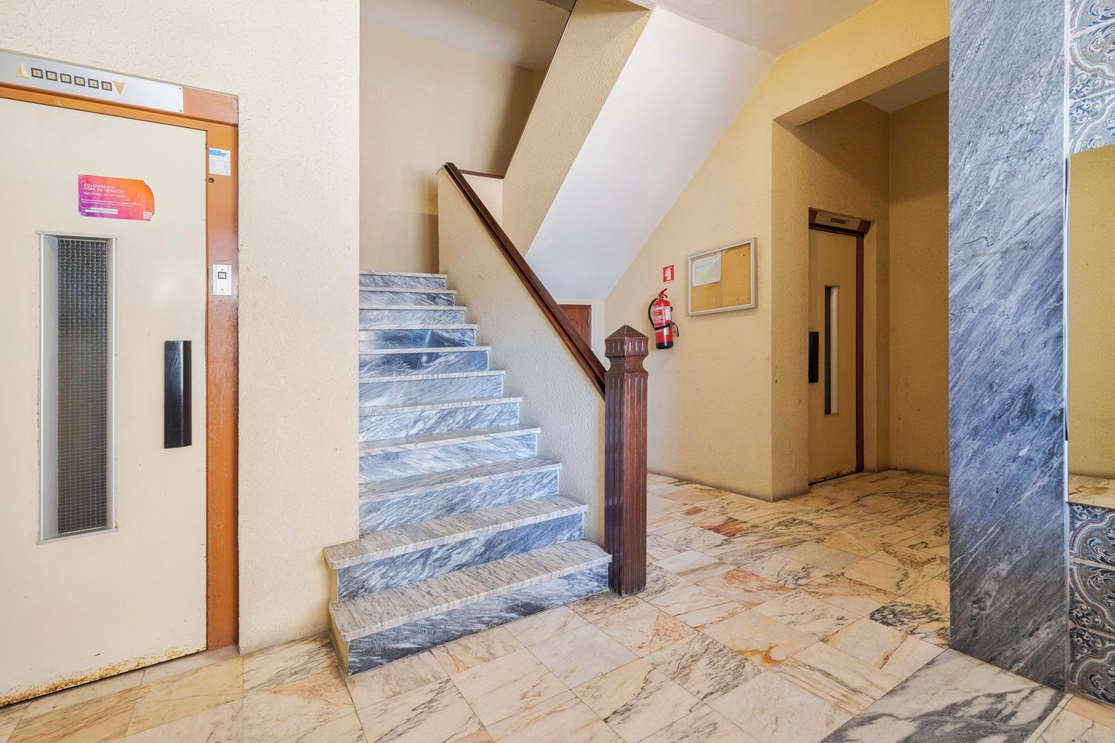 A marble staircase with a wooden handrail leading to an elevator.