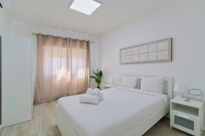 A hotel room with a bed, a nightstand, a bedside table, a potted plant, and a wall with framed artwork. - Bela House, By Home Match (Setúbal)