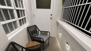 A small, enclosed outdoor space with a white door, two wicker chairs, a small table, and a window with a metal grill. - The Naguabeña House of the Anvil (Ceiba)