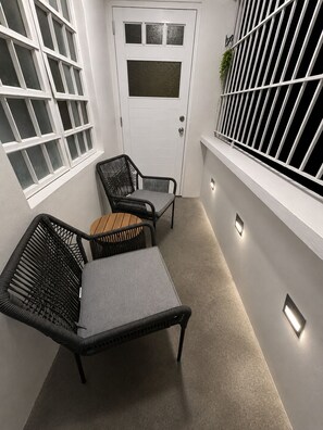 A small, enclosed outdoor space with a white door, two wicker chairs, a small table, and a window with a metal grill. - The Naguabeña House of the Anvil (Ceiba)