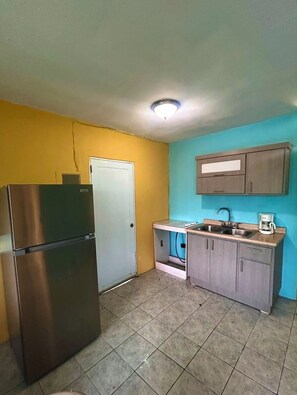 A compact kitchen with a stainless steel refrigerator, a white door, a sink with a faucet, and a coffee maker on the countertop. - The Naguabeña House of the Anvil (Ceiba)