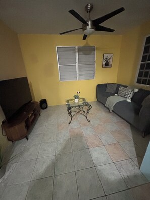 A living room with a ceiling fan, a sofa, a coffee table, and a television.