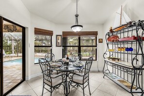 Un comedor interior con vista a la piscina, una mesa de comedor con sillas y una estantería metálica decorativa con cristalería.