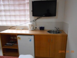 Una kitchenette compacta con refrigerador integrado, un lavamanos y un televisor montado en la pared.